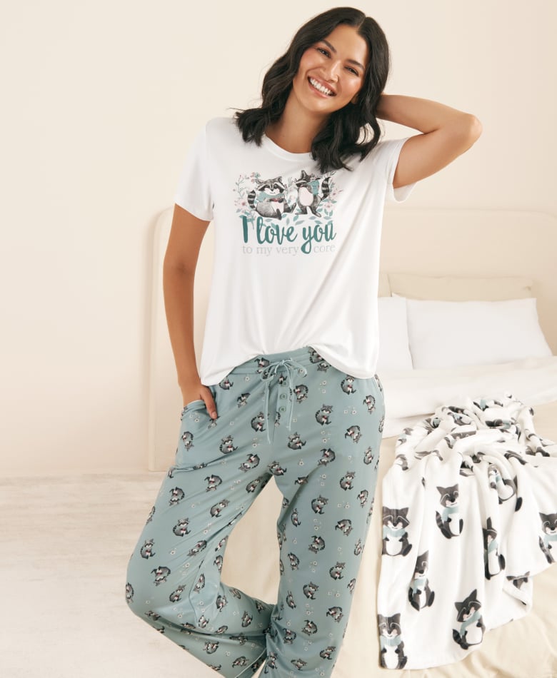 Model in pajamas with white t-shirt and blue pants with raccoon pattern.