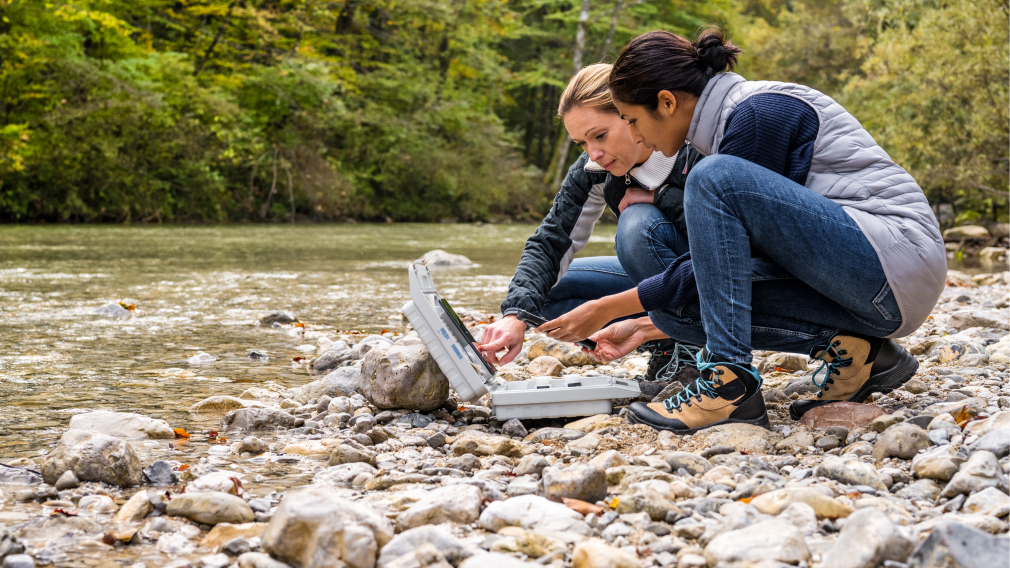 Two women standing by a river, testing the water quality
