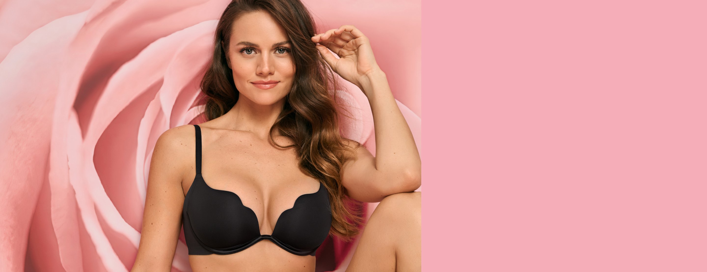 Model wearing a black scalloped push-up bra in front of a pink floral backdrop