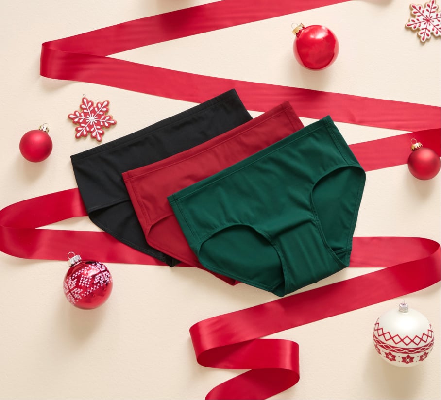 Three menstrual panties in red, black, and green displayed on a festive holiday setting.