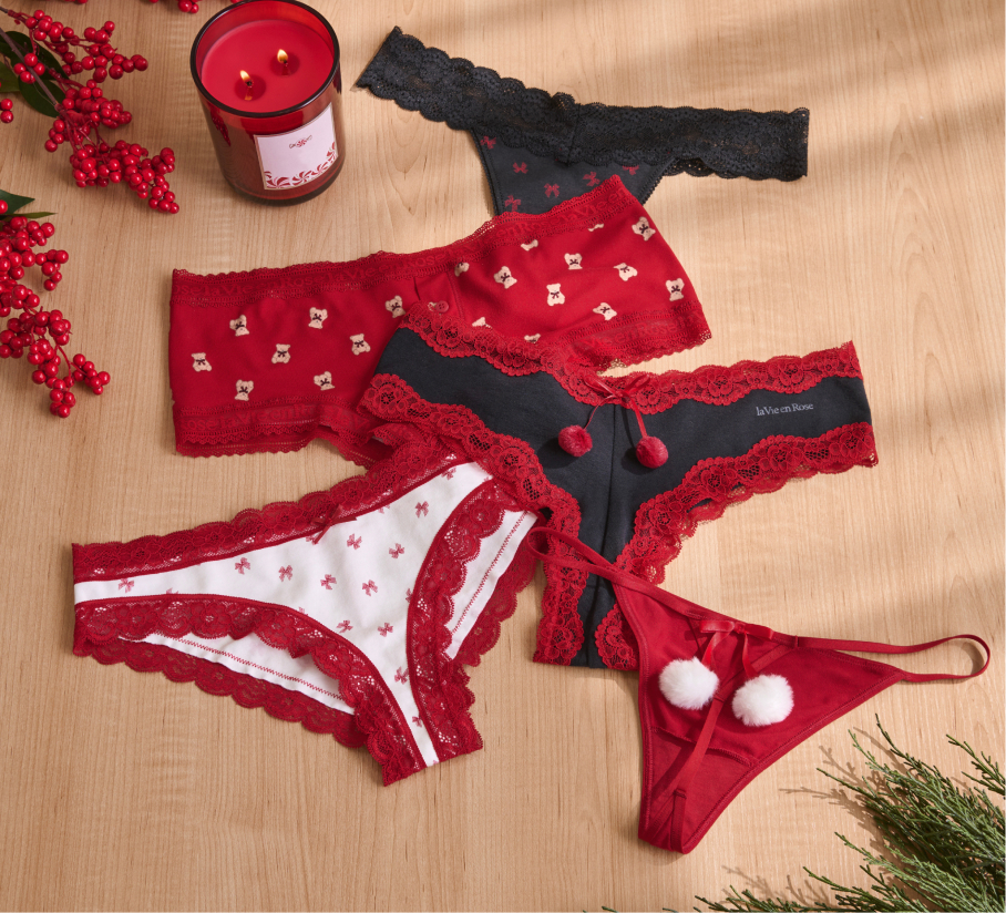 Set of festive lace panties in red, black, and white with holiday details, displayed on a wooden surface.