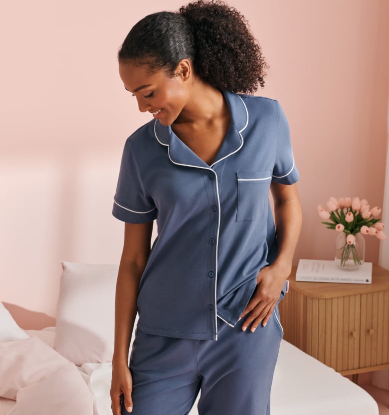 Banner linking to cotton pajama collection, model in blue set with short-sleeve shirt and matching pants.