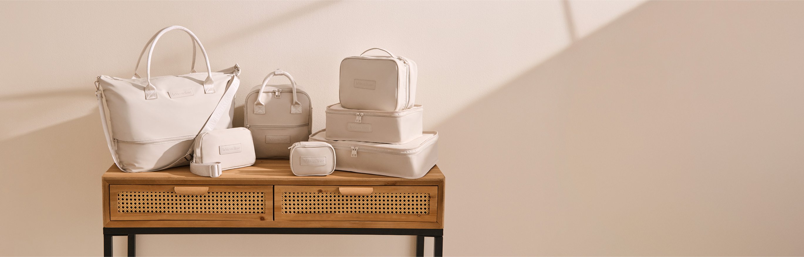 Seven beige travel accessories, including bags, pouches, and cases, placed on a table
