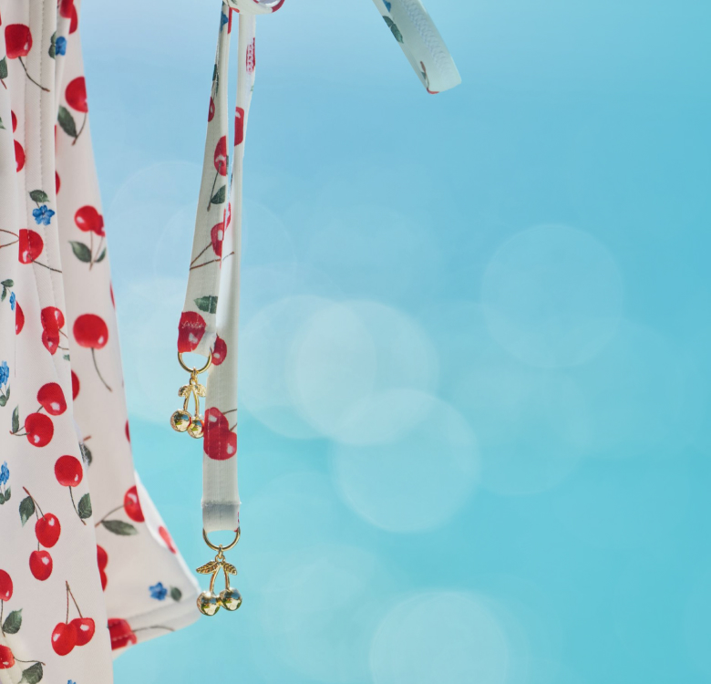 A model wearing a white bikini with a cherry pattern by the pool