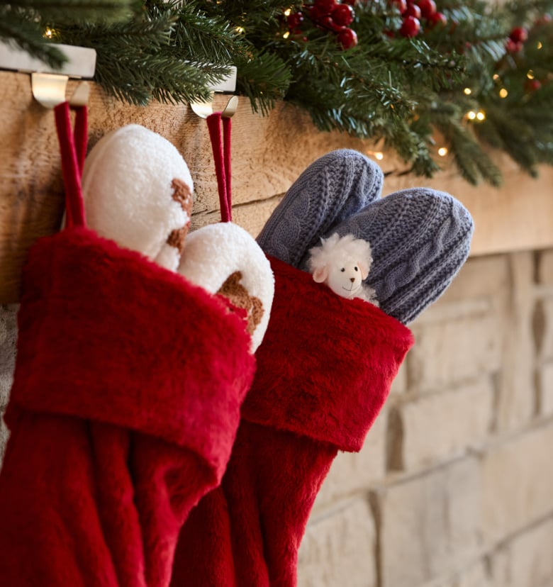 Red Christmas stockings hanging by a fireplace, filled with slippers