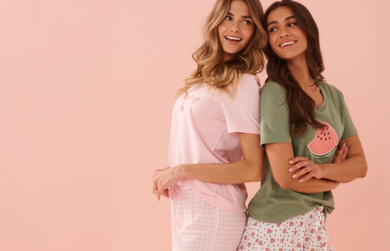 Two models in sleep t-shirts and shorts: one in light pink, the other in green with watermelon prints.