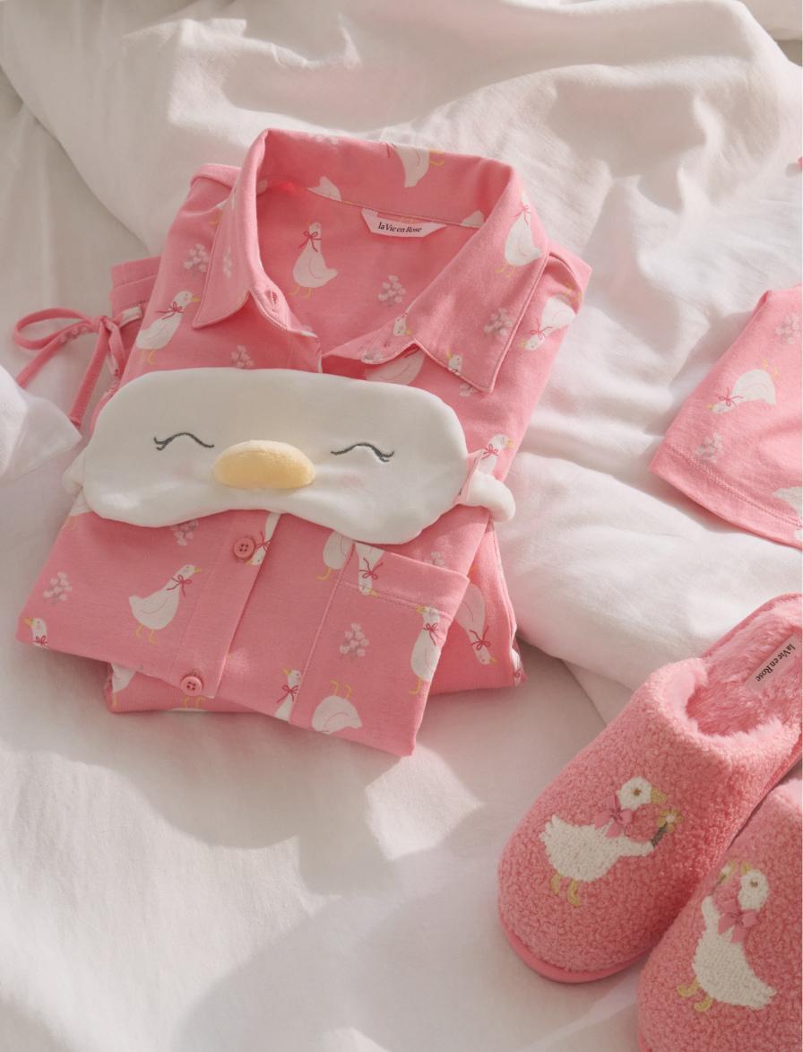 Pink pajamas with a goose print, folded up with the matching sleep mask and slippers next to them
