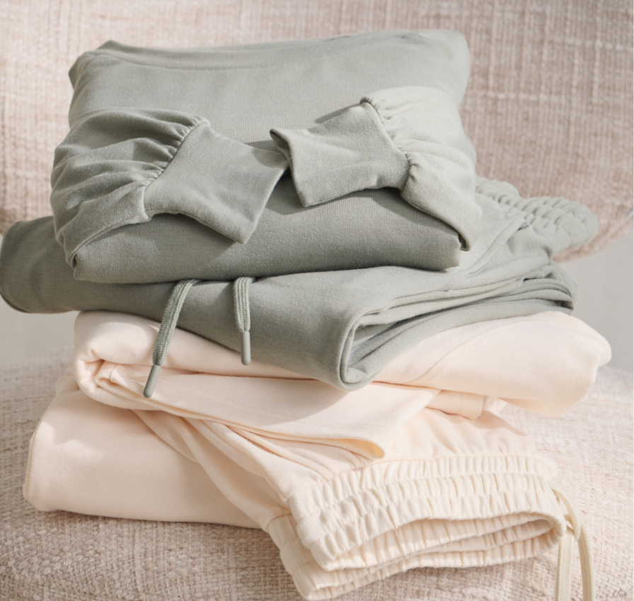 Two sets of loungewear folded on a chair, one sage green and the other pale yellow.