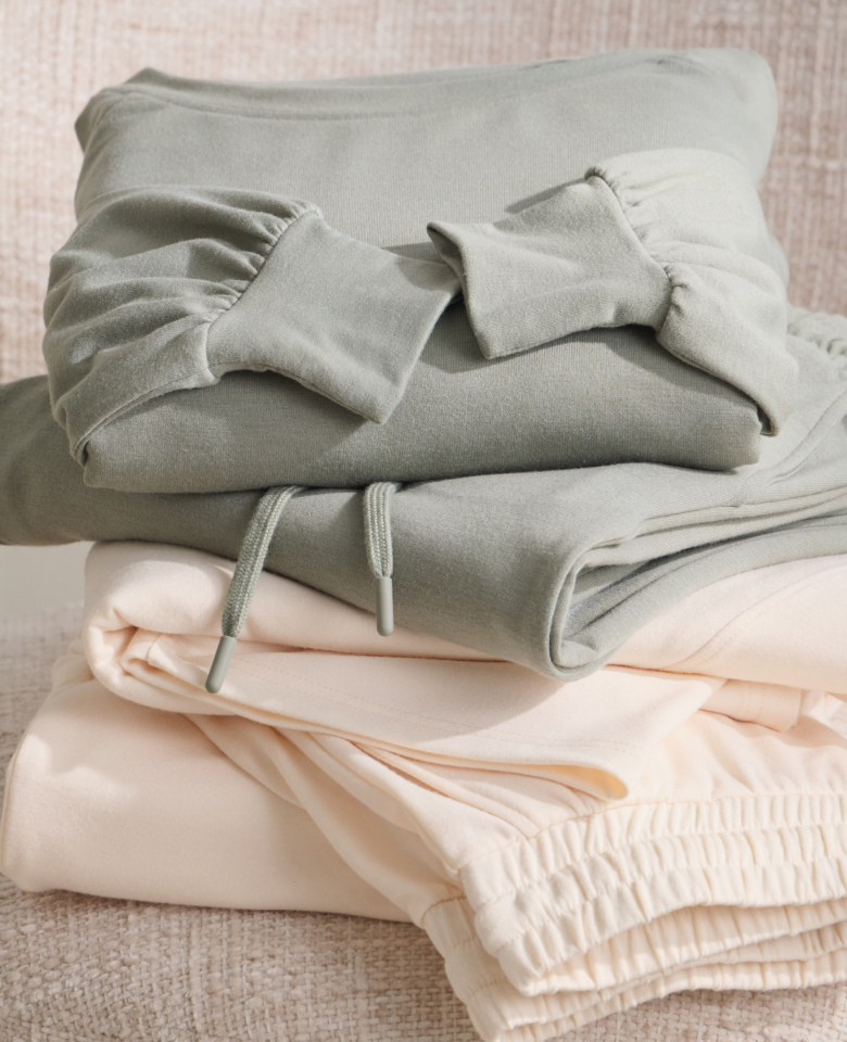 Two sets of loungewear folded on a chair, one sage green and the other pale yellow.