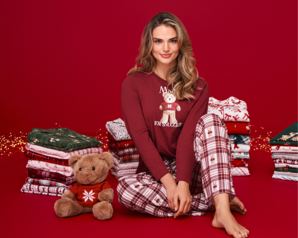 Model wearing a red pajama set, surrounded by stacks of pajamas