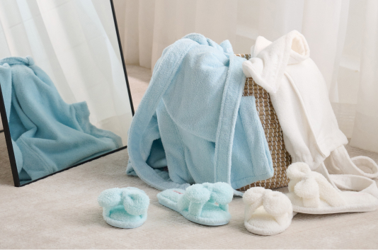 Deux peignoirs dans un panier, l'un blanc, l'autre bleu avec des chaussons assortis.