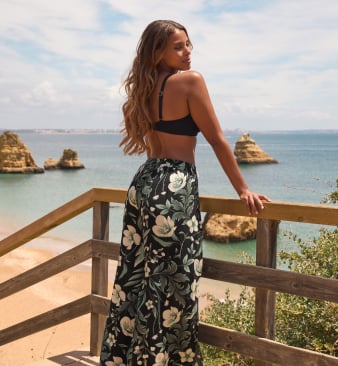 Model in black swim top and black beach pants with white flowers and printed foliage.