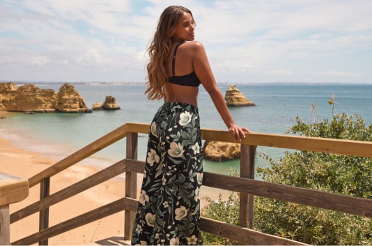 Model in black swim top and black beach pants with white flowers and printed foliage.