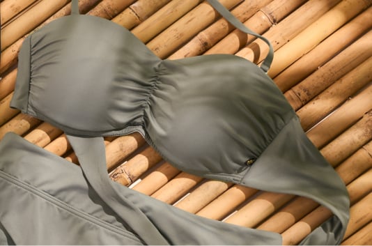  Sage green bandeau swimsuit top with matching bottom, laid on bamboo.