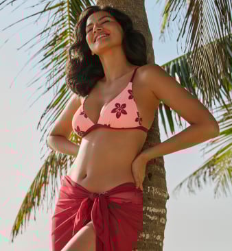 Model leaning against a palm tree, wearing a pink floral triangle bikini top, illustrating the Summer Romance trend. 