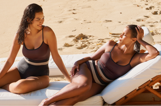 Two models in brown bikinis and one-piece swimsuits