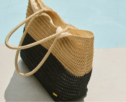 Black and beige straw beach tote by a poolside.