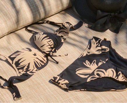 Black bikini set with beige floral print laid flat on a beach chair.
