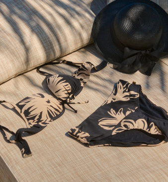 Black bikini set with beige floral print laid flat on a beach chair.